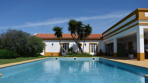 Una piscina amb un edifici al fons, palmeres i un cel serè.