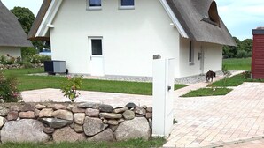 Ein Haus mit einem Strohdach, einer Steinmauer davor und einem gepflasterten Einfahrtsweg.