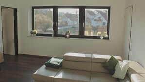Et værelse med et stort vindue, en beige sofa og et lille bord.