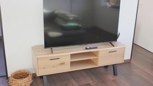 Et fladskærms-TV på et træ TV-bord med to skuffer og en hylde, placeret i et rum med trægulv.