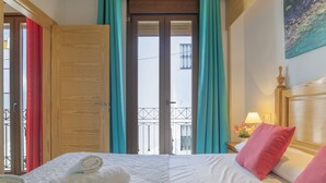 A hotel room with a bed, a nightstand, a lamp, and a view of the outside.