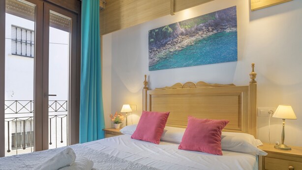 A hotel room with a bed, two bedside lamps, a painting, and a view of a balcony.