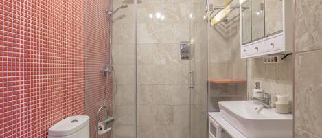 Een badkamer met toilet, douche, wastafel en spiegel.