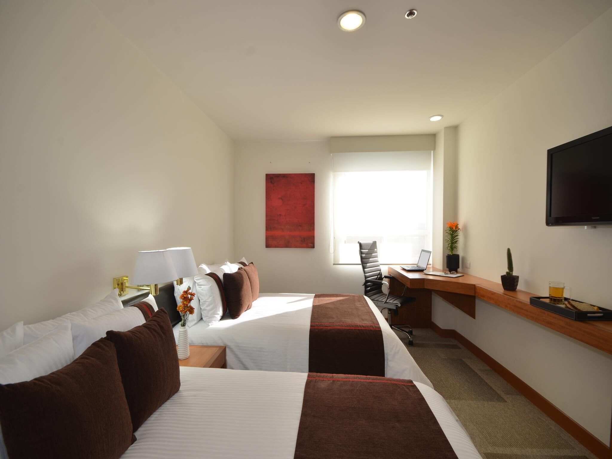 A hotel room with two beds, a desk with a laptop, a television, and a window with a view.