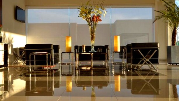 A spacious lobby with a reflective floor, a central floral arrangement, and seating areas with tables and chairs. - Hotel Lois Express Monterrey Aeropuerto La Fe (Apodaca)