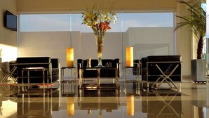 A modern lobby with a reflective floor, black leather seating, a tall vase with flowers, and a large window. - Hotel Lois Express Monterrey Aeropuerto La Fe (Apodaca)
