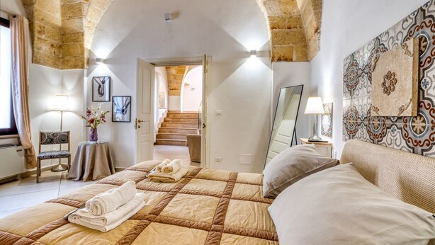 Habitació d'hotel amb un llit gran, una cadira, una taula i una escala que condueix a una altra habitació.