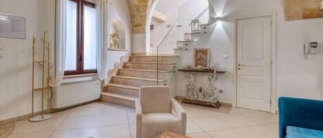 A spacious living area with a staircase, a blue sofa, a beige armchair, and a wooden coffee table.