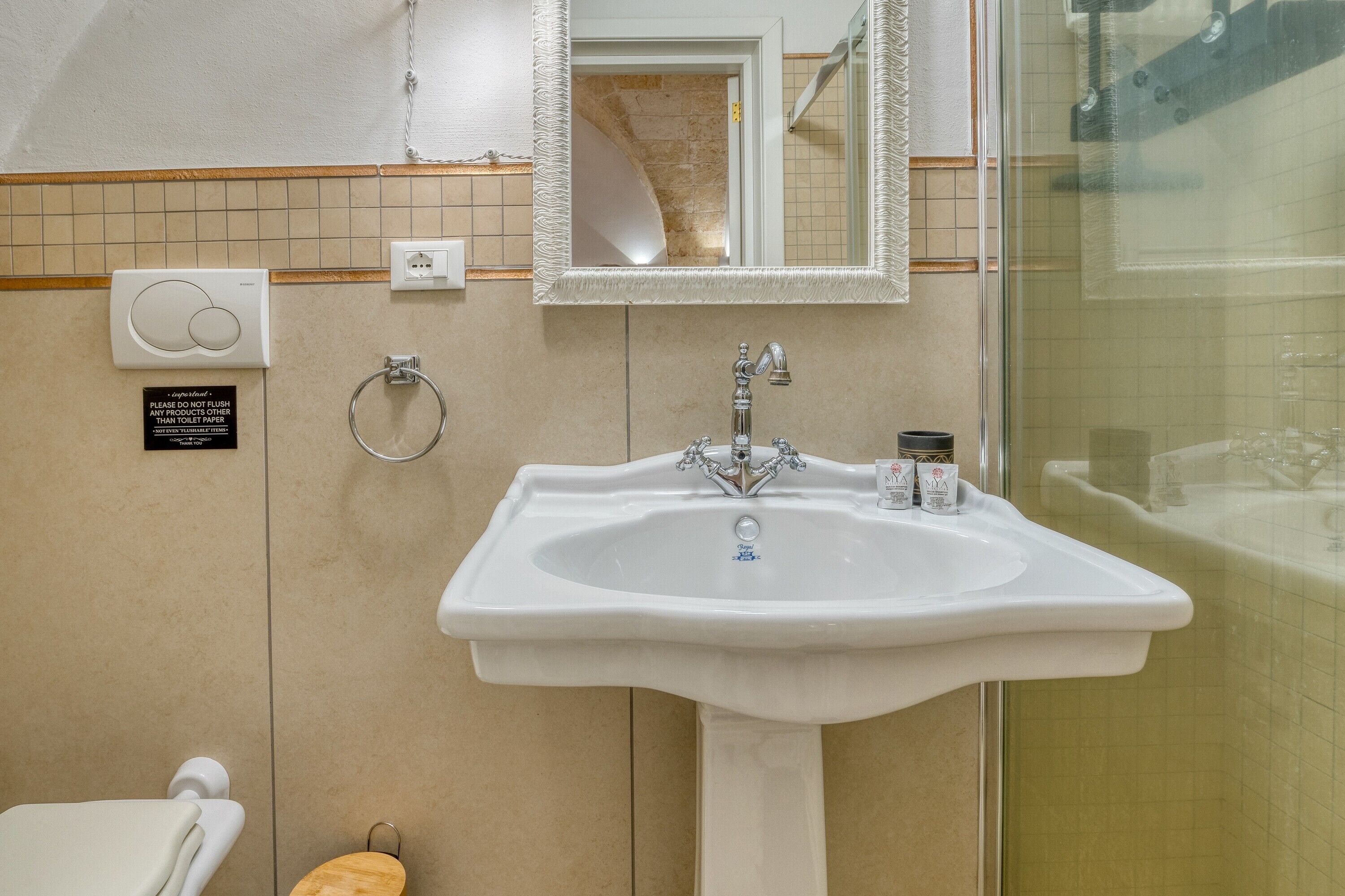 Un bagno con un lavandino su piedistallo, uno specchio, un porta asciugamani e un cartello che indica di non gettare la carta igienica nel WC.