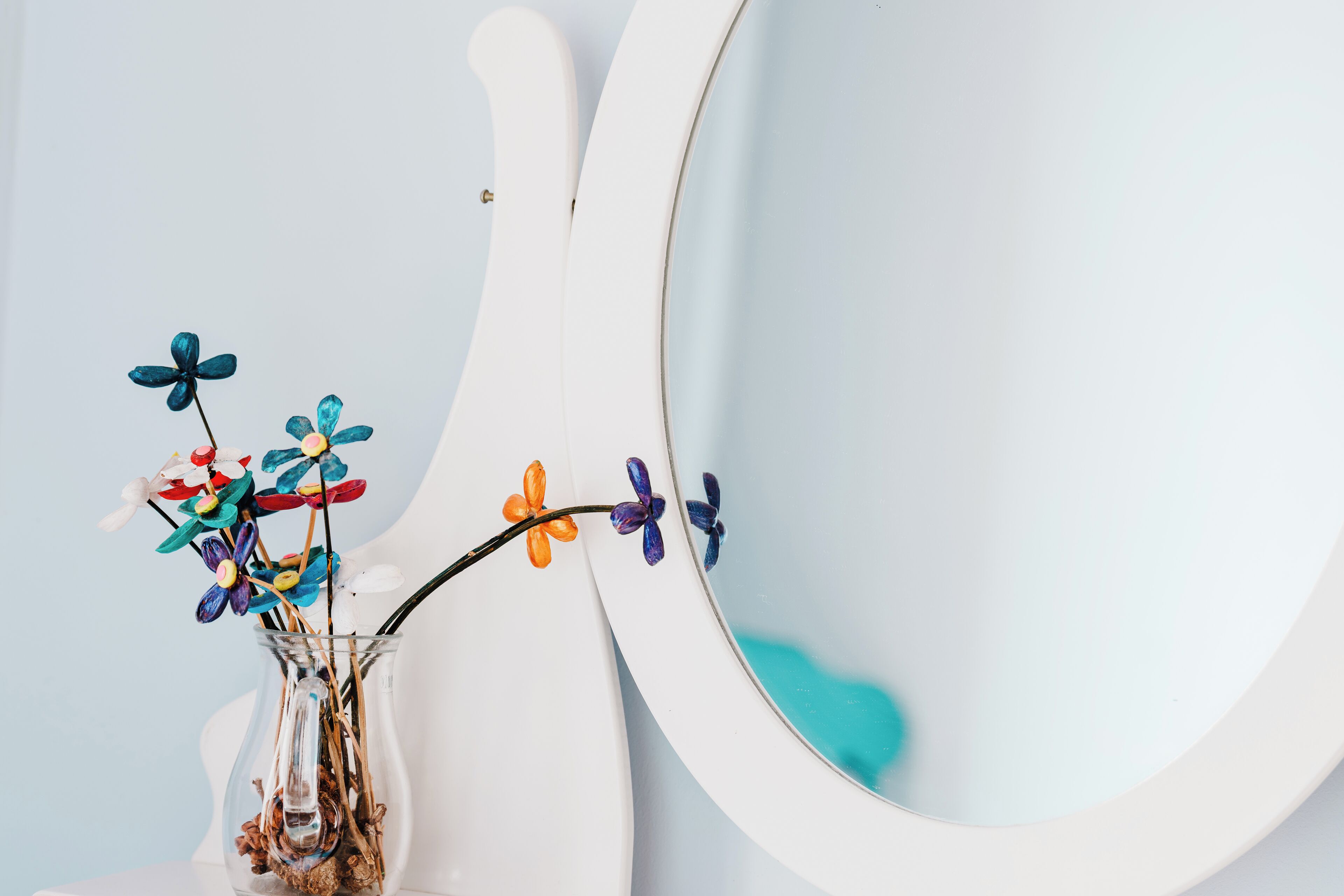 A bathroom with a white sink, a mirror, and a vase with colorful flowers.