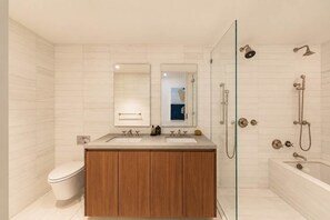 Ein modernes Badezimmer mit einem Holzbadezimmer-Möbel, zwei Waschbecken, einer Toilette, einer in Glas eingefassten Dusche und einem großen Spiegel.
