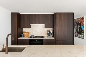 A modern kitchen with dark wood cabinets, a marble countertop, a gas stove, and a coffee machine. - Nolita Duplex by StayHaus | 3BR w/ Private Garden (New York)