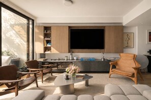 Ein modernes Wohnzimmer mit Couch, Sesseln und Fernseher.
