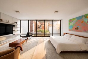 Ein modernes Schlafzimmer mit einem großen Bett, einem Fernseher, einer Couch und Blick ins Freie.