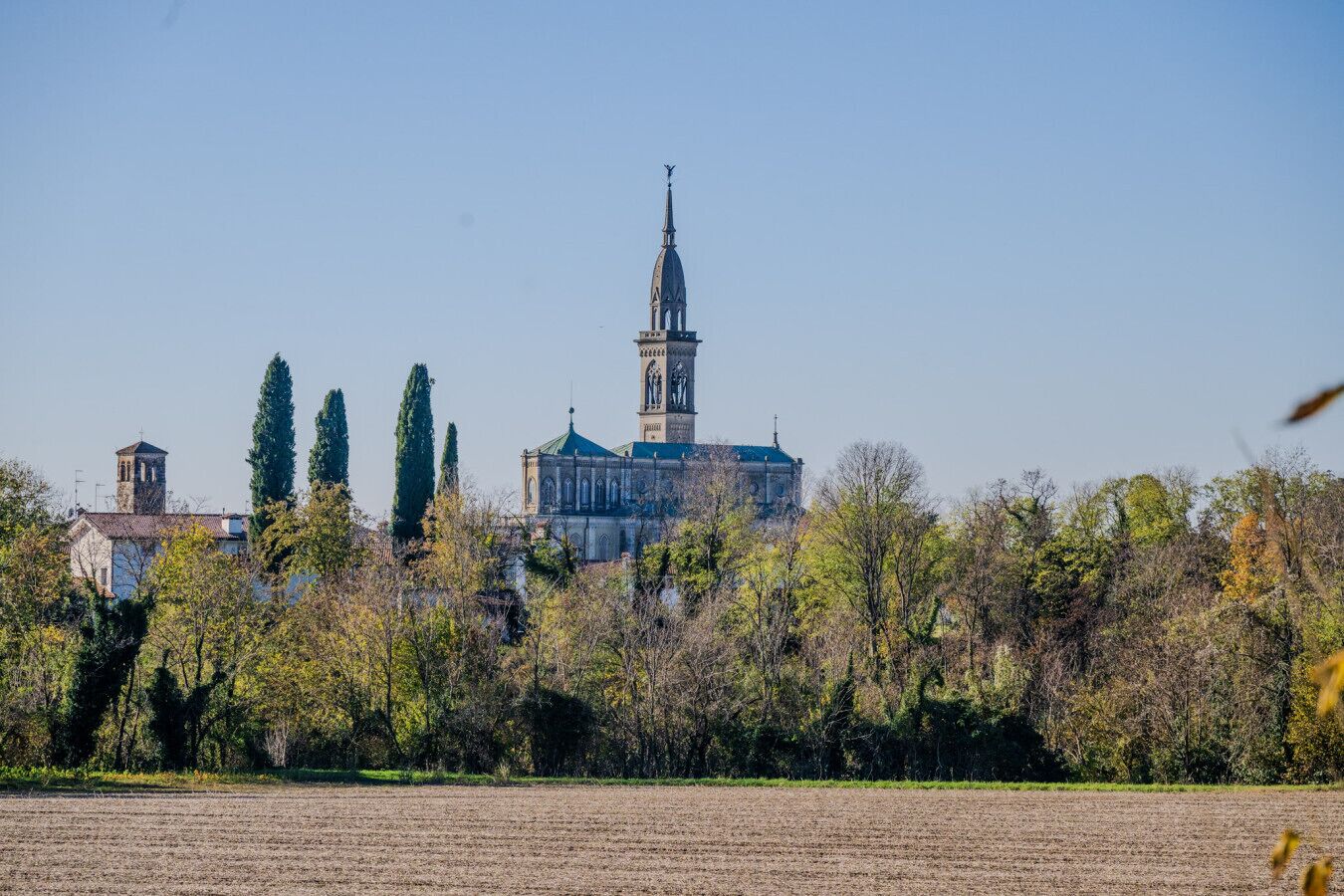 Une grande église dotée d’un imposant clocher et d’une flèche, entourée d’arbres et d’un champ.