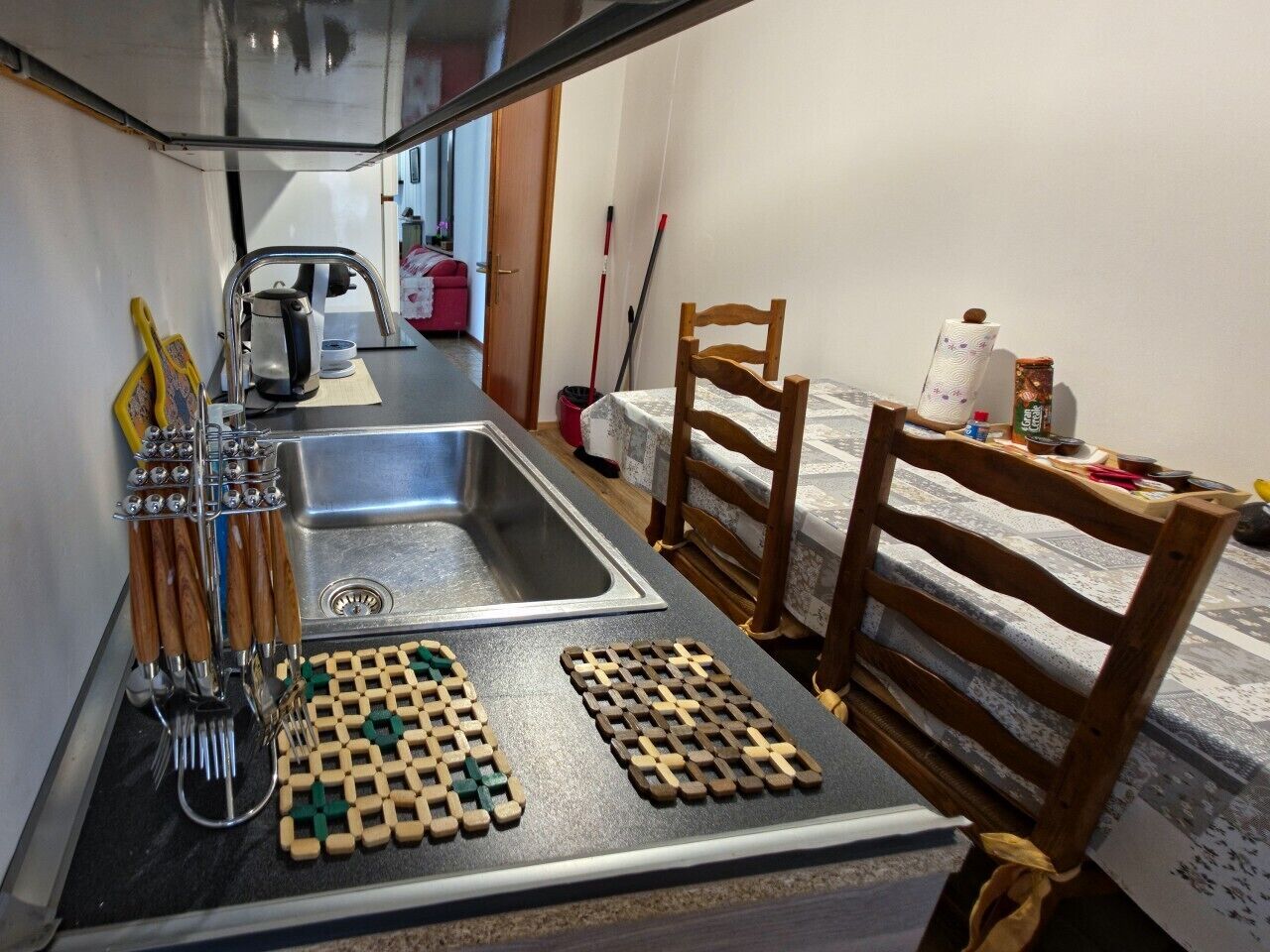 Cocina compacta con un lavamanos, utensilios de madera y un tablero de ajedrez.