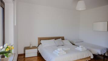 Une chambre à coucher avec un lit en bois, du linge de lit blanc, une table de chevet avec une lampe et une petite table de nuit ornée d’un vase de fleurs.