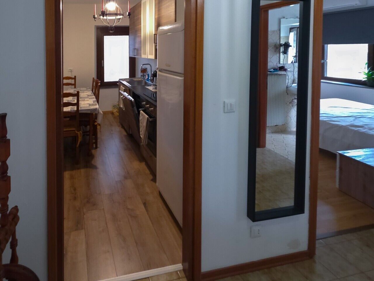 Un corridoio stretto che conduce a una zona pranzo con tavolo e sedie, una cucina con frigorifero, e un letto nella stanza adiacente.