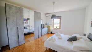 Ein modernes Schlafzimmer mit einem großen Bett, einem Kleiderschrank mit Spiegeln, einem kleinen Schreibtisch und einem Fenster mit Blick.