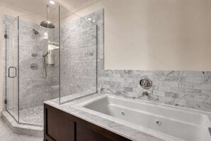 Un baño con ducha envuelta en vidrio, pared con azulejos de mármol y bañera independiente.