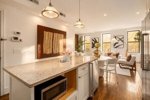 A modern kitchen with a granite countertop, built-in microwave, pendant lighting, and a dining area with a white table and chairs. - Madison I by StayHaus | Full-floor Flatiron 2BR (New York)