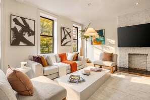A modern living room with a fireplace, large windows, and artwork on the walls. - Madison I by StayHaus | Full-floor Flatiron 2BR (New York)