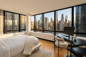 A bedroom with a city view, a bed, a desk, and a chair. - Skyline V | 26th-floor 3BR w/Doorman, Gym, and Pool (New York)