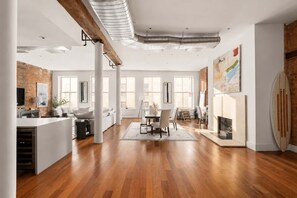 A spacious living area with a dining table, white sofas, and a fireplace. - Greene Loft by StayHaus | 3BR w/ Doorman, Elevator (New York)