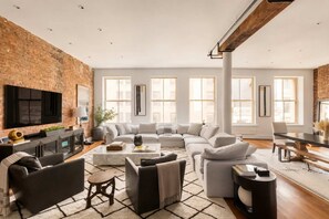 A spacious living room with a large sectional sofa, a flat-screen TV, and a fireplace. - Greene Loft by StayHaus | 3BR w/ Doorman, Elevator (New York)
