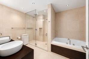 A modern bathroom with a glass-enclosed shower, a freestanding bathtub, and a vanity with two sinks. - Greene Loft by StayHaus | 3BR w/ Doorman, Elevator (New York)