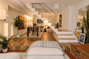 A modern living room with a staircase, a dining area, and a cozy seating area. - Clinton Duplex by StayHaus | 2BR with Private Yard (Brooklyn)