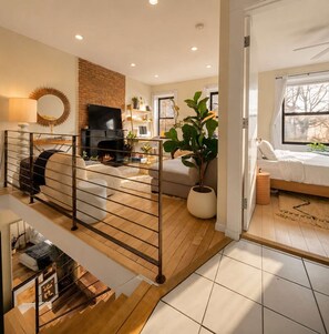 A modern living room with a fireplace, a TV, and a staircase leading to another room. - Clinton Duplex by StayHaus | 2BR with Private Yard (Brooklyn)