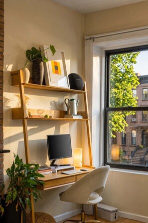 A modern workspace with a desk, chair, computer, and shelves with various items. - Clinton Duplex by StayHaus | 2BR with Private Yard (Brooklyn)