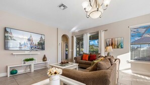 A living room with a flat-screen TV, a sofa, a coffee table, and a TV stand with a plant. - 4163 Oak Tree Drive (Davenport)