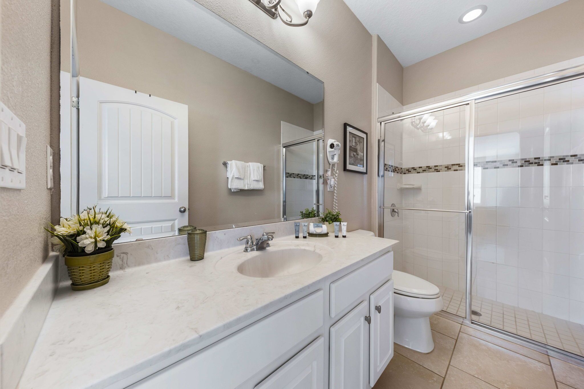 Une salle de bain avec un lavabo blanc, des toilettes, une douche en verre et un grand miroir.