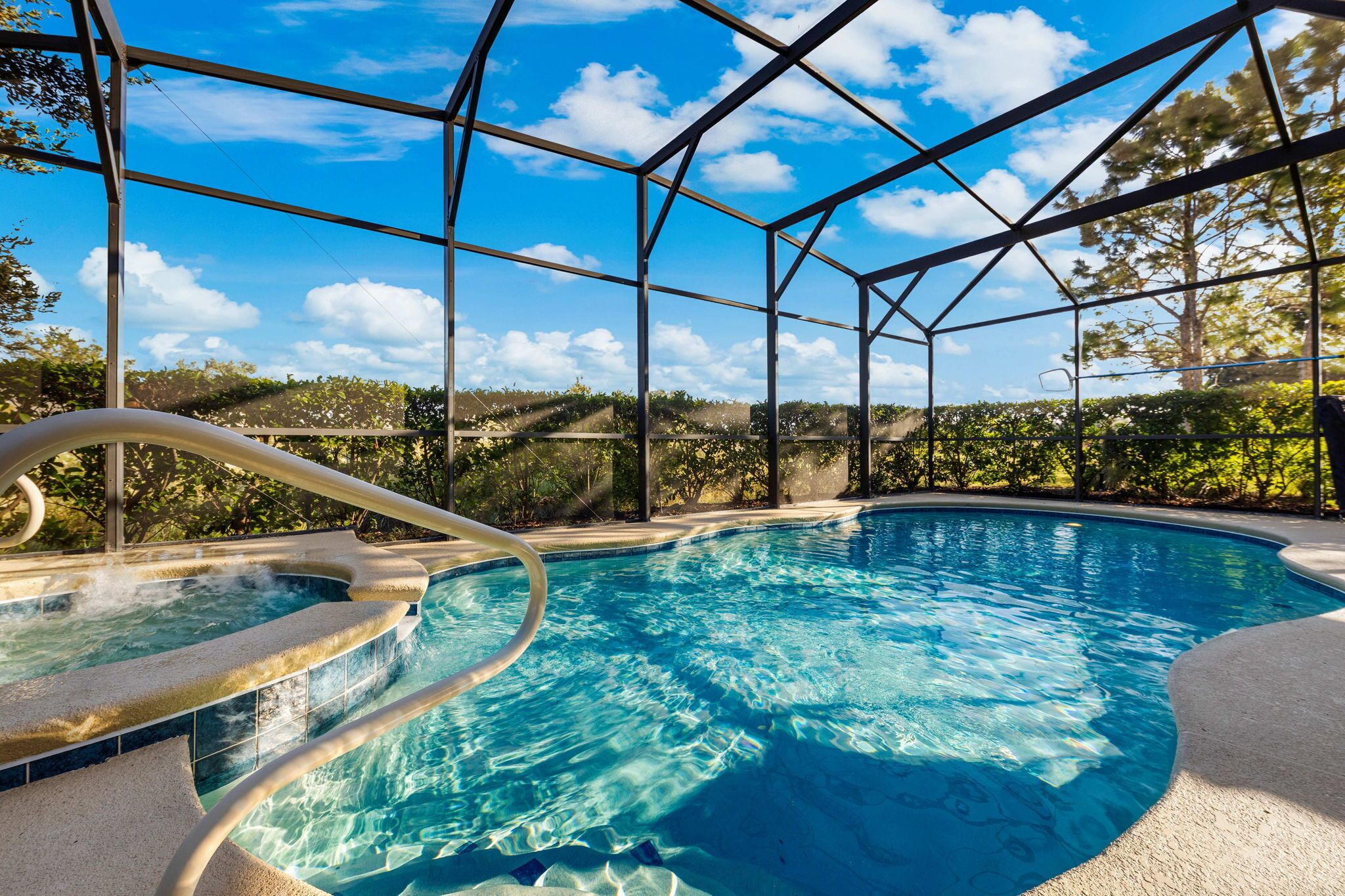 Piscina azul translúcida com estrutura de vidro, rodeada por árvores e céu claro.