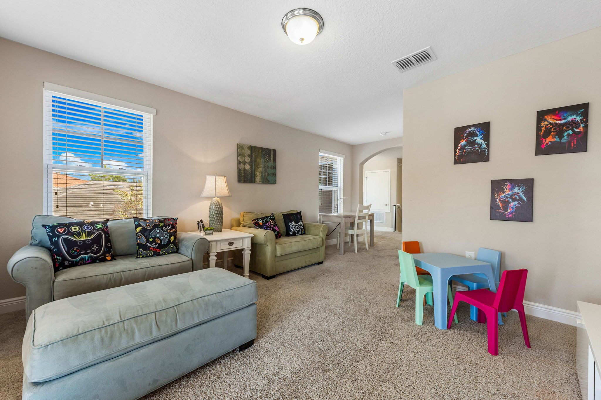 A living room with a grey sofa, a green armchair, a small table with a lamp, and a children's table with colorful chairs.
