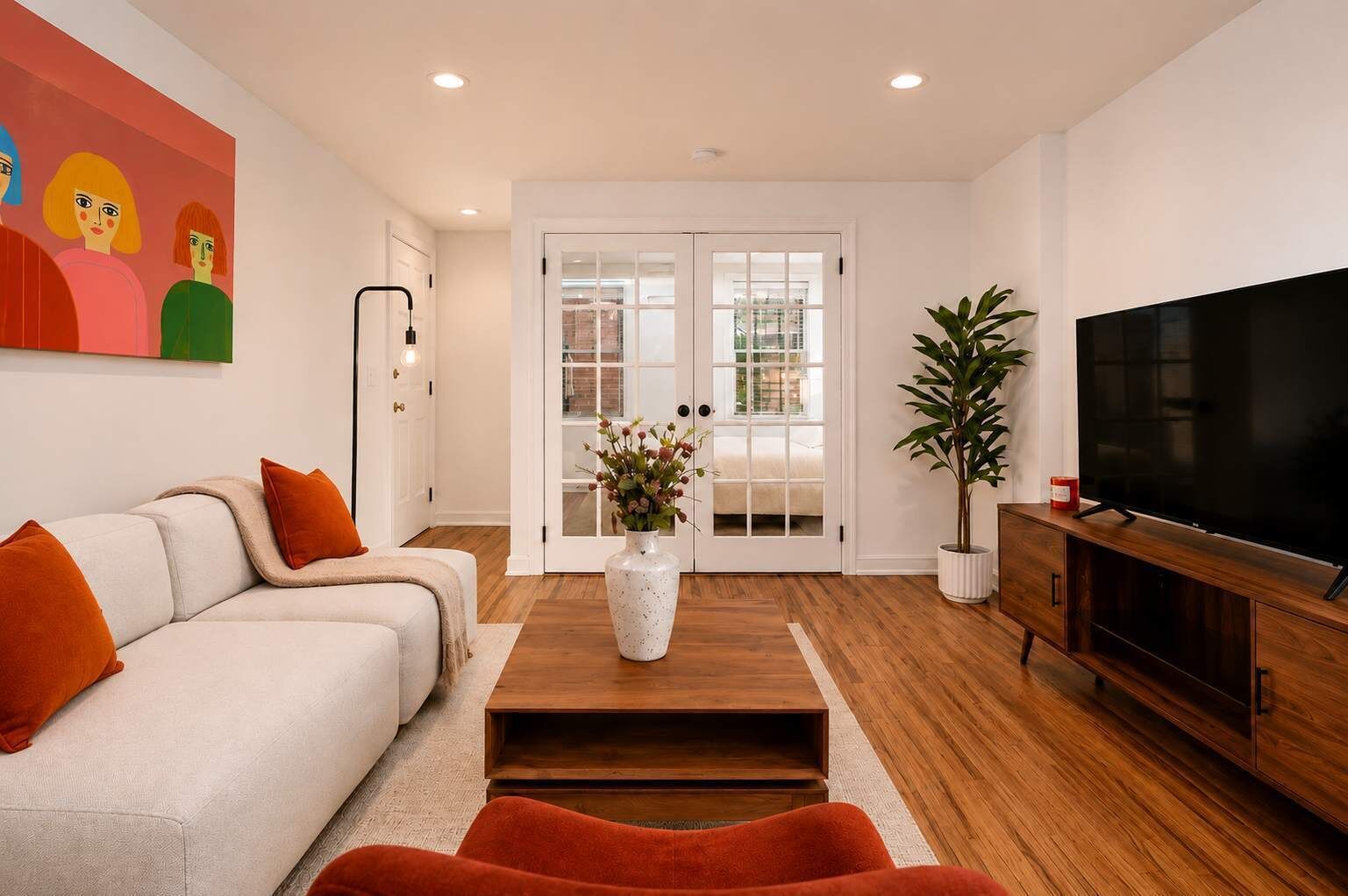 A modern living room with a sofa, coffee table, TV, and a door leading outside.