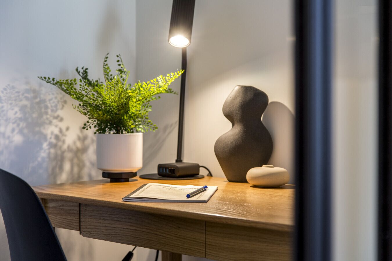 Een houten bureau met een plant in pot, een moderne lamp en een decoratieve vaas.
