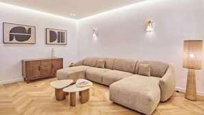 A modern living room with a sectional sofa, wooden herringbone flooring, a cabinet, and two small tables. - Charming apartment - Canal Saint-Martin (Paris)
