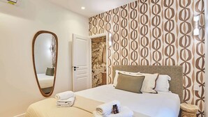 A hotel room with a large bed, a wooden headboard, a mirror, and patterned wallpaper. - Charming apartment - Canal Saint-Martin (Paris)