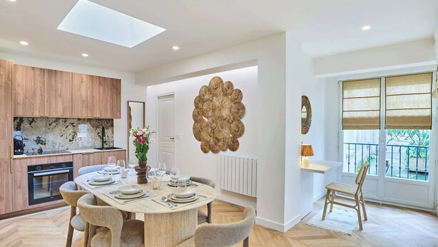A modern kitchen with wooden cabinets, a built-in oven, and a dining area with a round table and chairs. - Charming apartment - Canal Saint-Martin (Paris)