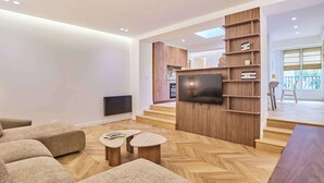 A modern living room with a flat-screen TV mounted on a wooden wall, a herringbone-patterned wooden floor, and a sofa with a matching ottoman. - Charming apartment - Canal Saint-Martin (Paris)