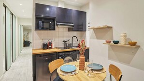 A compact kitchen with a microwave, toaster, and sink. There is a dining area with a round table and chairs. - Spacious Studio Sacre Coeur-Montmartre (Paris)