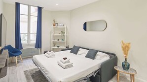 A modern hotel room with a large bed, a desk, a chair, a small table, a mirror, and a window with curtains. - Spacious Studio Sacre Coeur-Montmartre (Paris)