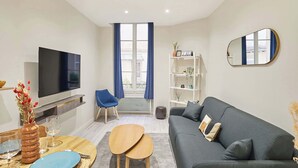 A modern living room with a flat-screen TV, a blue chair, a grey sofa, and a white shelving unit. - Spacious Studio Sacre Coeur-Montmartre (Paris)