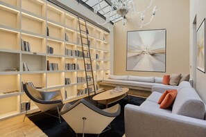 A modern living room with a bookshelf, a sofa, a coffee table, and a chandelier. - A modern and unique loft - Center of Paris (Paris)