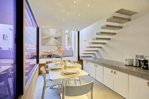 A modern kitchen with a built-in staircase, dining area with a table set for two, and a view through a glass door. - A modern and unique loft - Center of Paris (Paris)