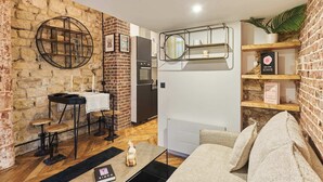 A compact living space with a brick wall, a round metal shelf, a small dining table, and a sofa. - Charming Apartment - Paris Pere Lachaise (Paris)