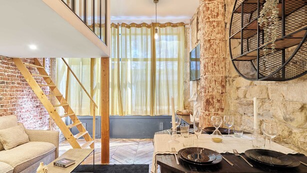 A dining area with a table set for two, a wooden staircase, and a brick wall. - Charming Apartment - Paris Pere Lachaise (Paris)
